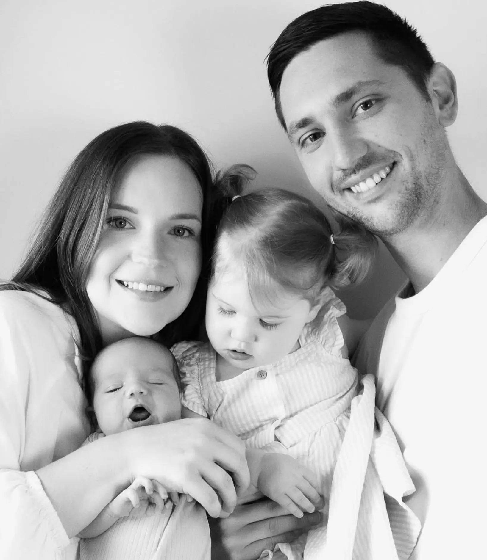 Parents and a toddler holding a sleeping newborn, black and white portrait