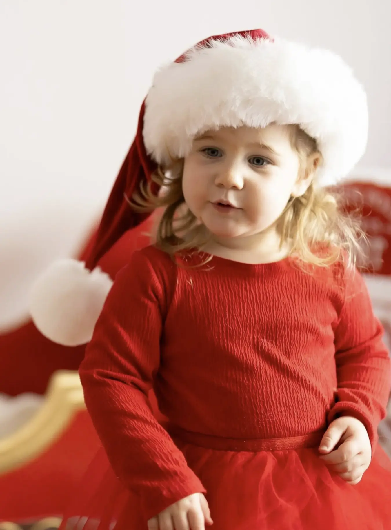 Young girl in a red dress and Santa hat sitting in a Christmas sleigh