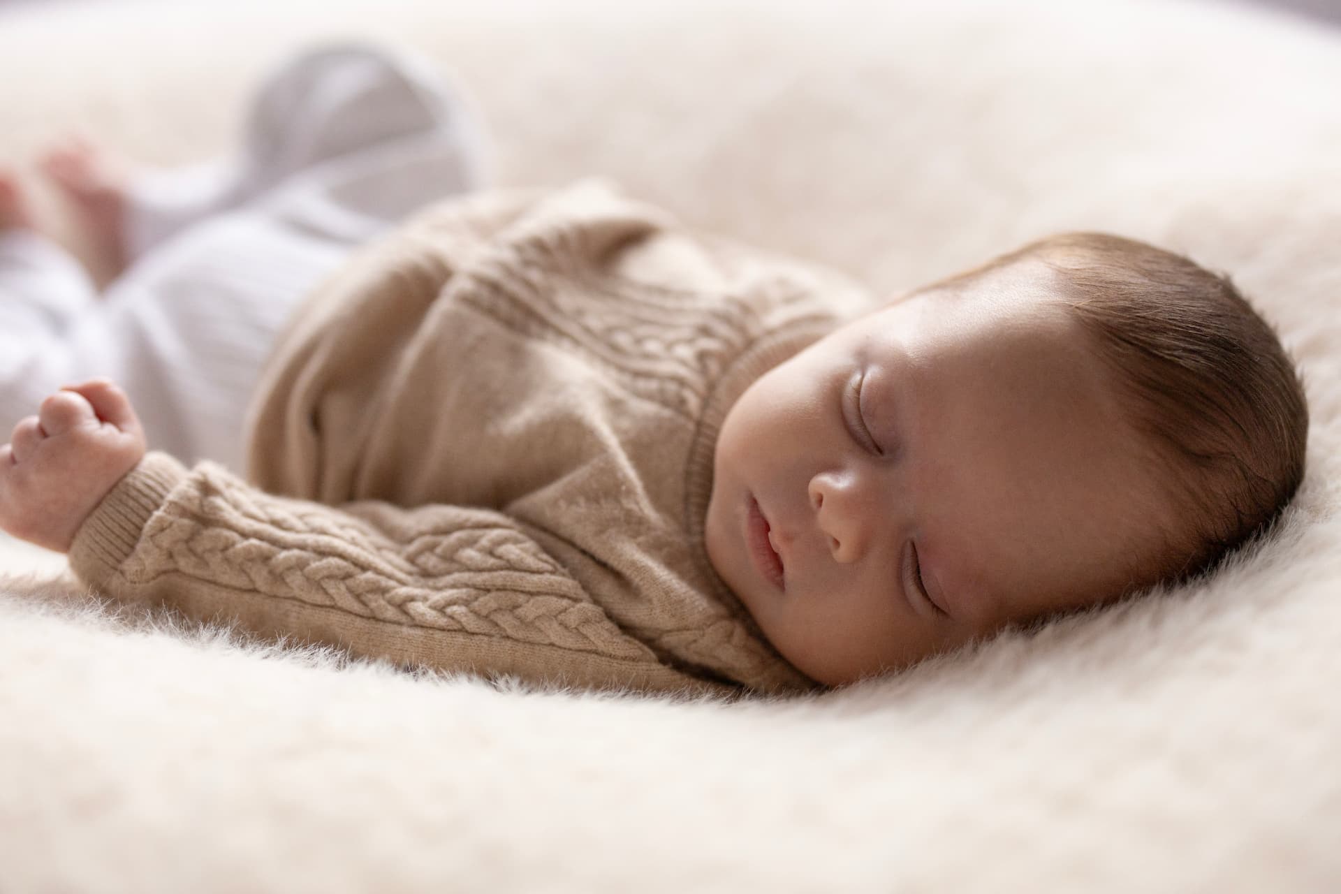 Newborn baby sleeping in a knitted cardigan on soft cream fur
