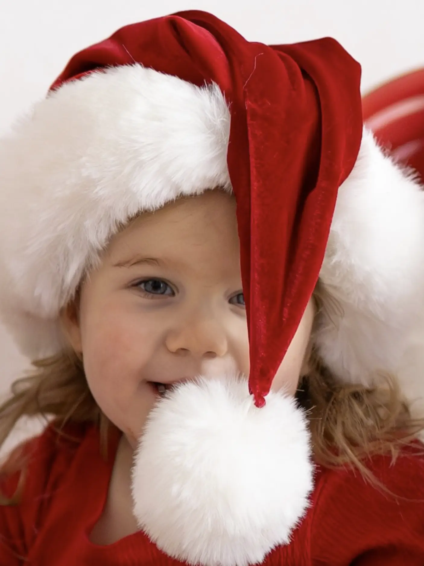 Close up of a young girl smiling under a red Santa hat