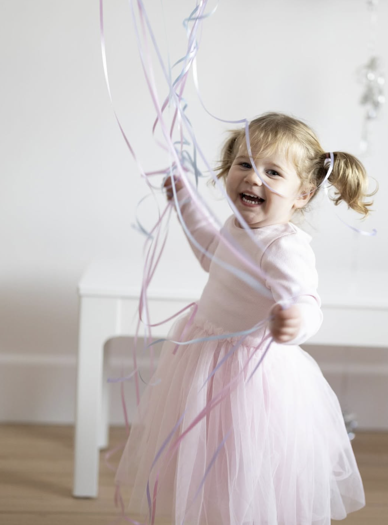 Young girl in a pink tulle dress laughing among falling ribbons