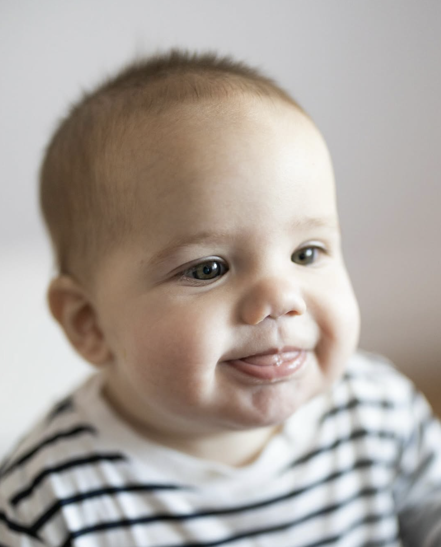Baby in a striped top smiling in a bright in-home studio
